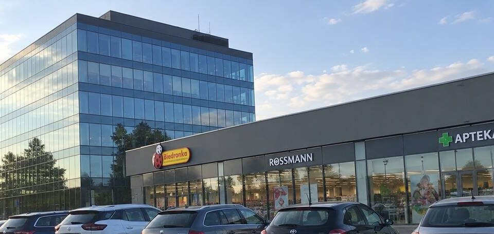 Przeszklony biurowiec i pawilon handlowy z witrynami przy parkingu z samochodami
