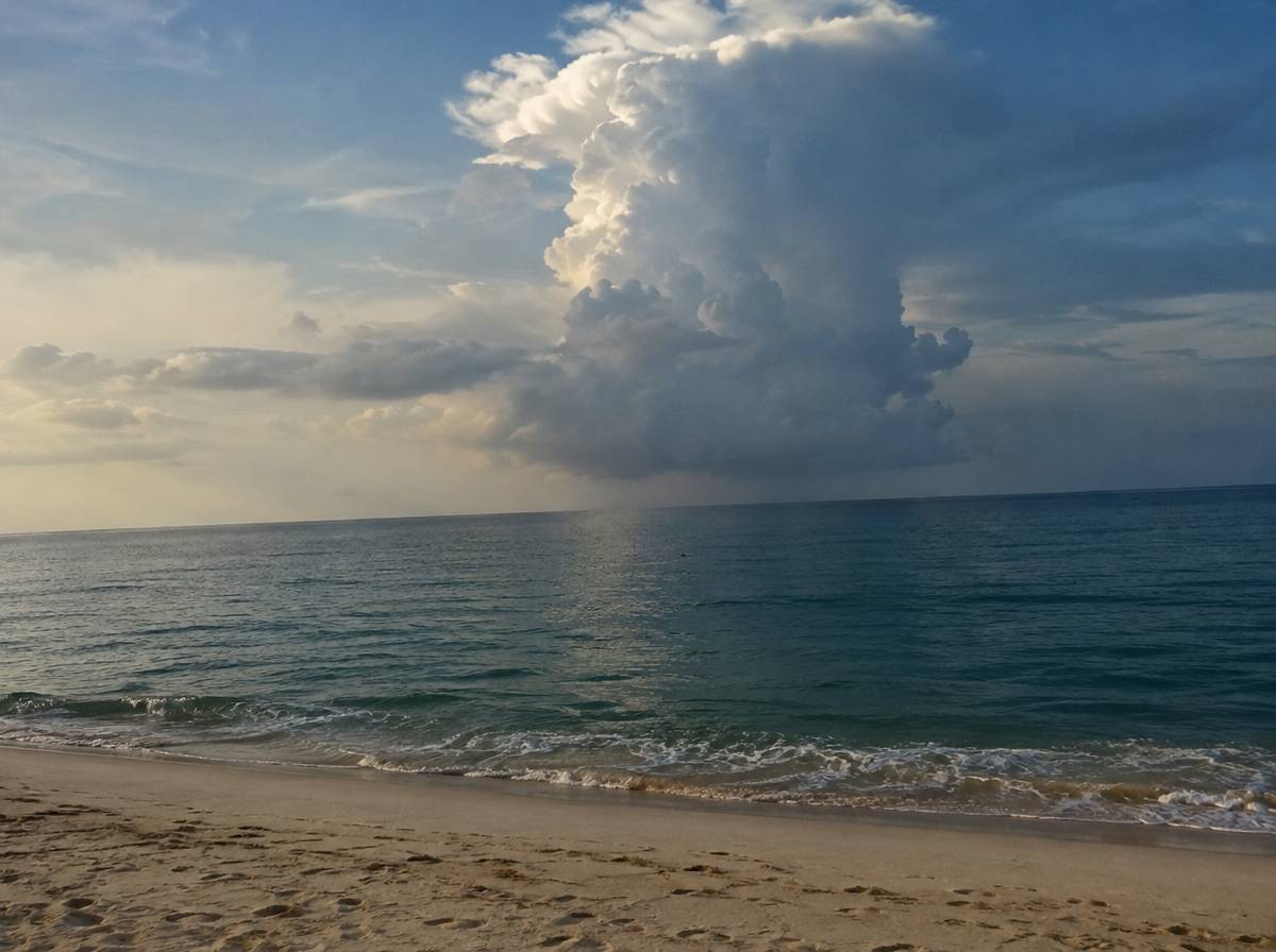 Skupisko chmur burzowych cumulonimbus nad spokojnym tropikalnym oceanem widziane z piaszczystej plaży