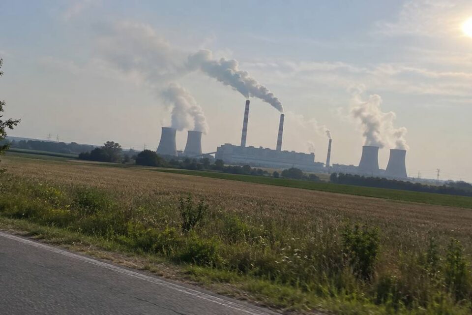 Elektrownia węglowa z dymiącymi kominami i chłodniami kominowymi za polami w letni dzień