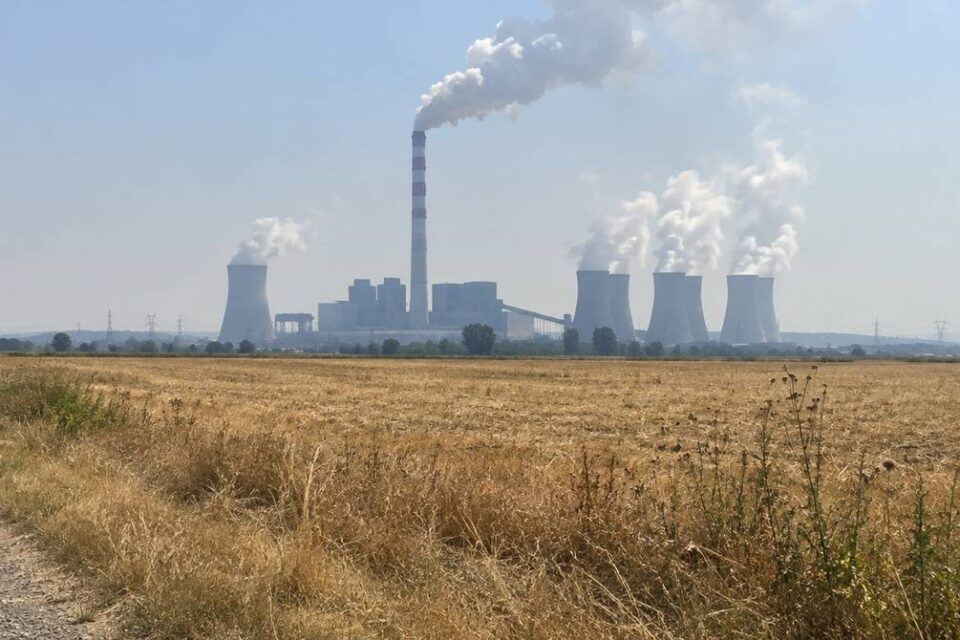 Elektrownia węglowa z kominem i chłodniami kominowymi za wysuszonym polem w letnim upale
