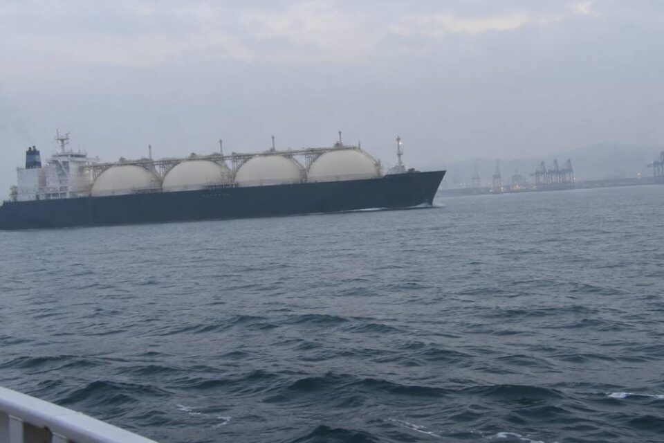 Gazowiec LNG z kulistymi zbiornikami płynie po morzu w pobliżu portu z żurawiami