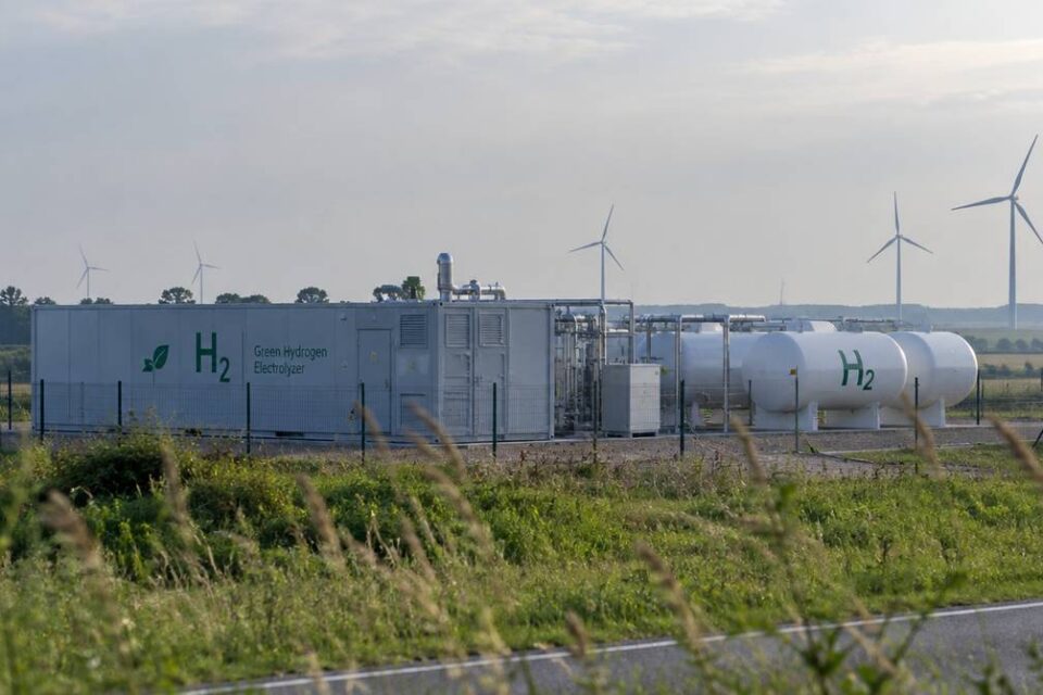 Instalacja zielonego wodoru z elektrolizerem w kontenerze i zbiornikami na wodór, w tle turbiny wiatrowe