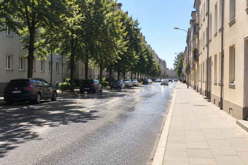 Śródmiejska ulica w upale, rozgrzany asfalt i beton w słońcu, po jednej stronie cień drzew liściastych
