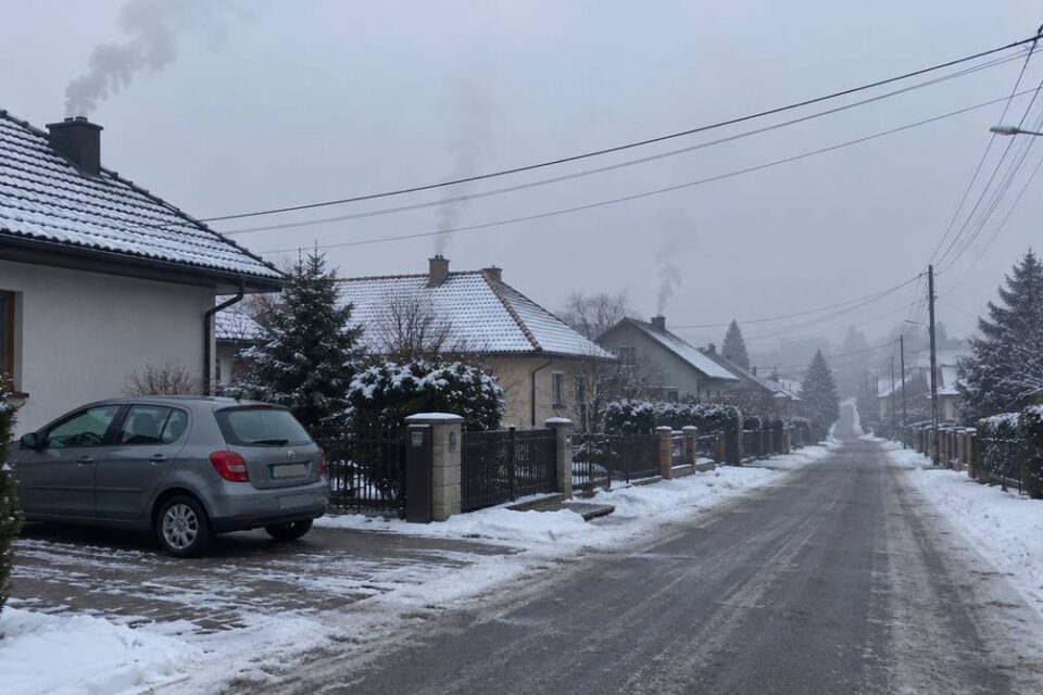 Osiedle domów jednorodzinnych zimą, dym z kominów nad dachami i samochód na podjeździe