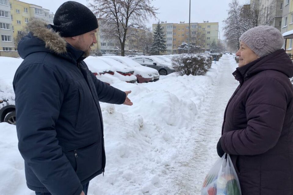 Mężczyzna wskazuje na zaspy śniegu w rozmowie z sąsiadką na zimowym osiedlu