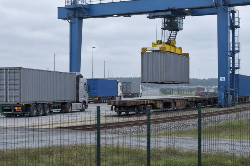 Suwnica bramowa w terminalu intermodalnym przenosi kontener z naczepy ciężarówki na wagon pociągu towarowego