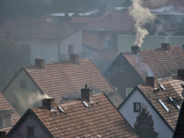 Ciemny dym ulatujący z komina na dachu domu